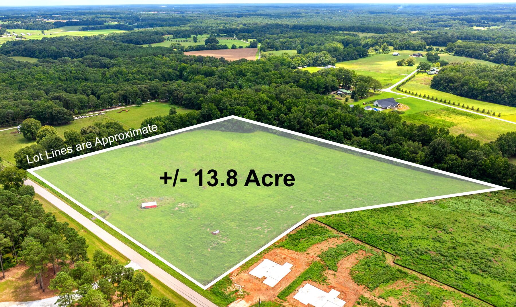 Drone view of the green fenced pasture outlined in white along a paved road, new house slabs on the neighbouring lots.