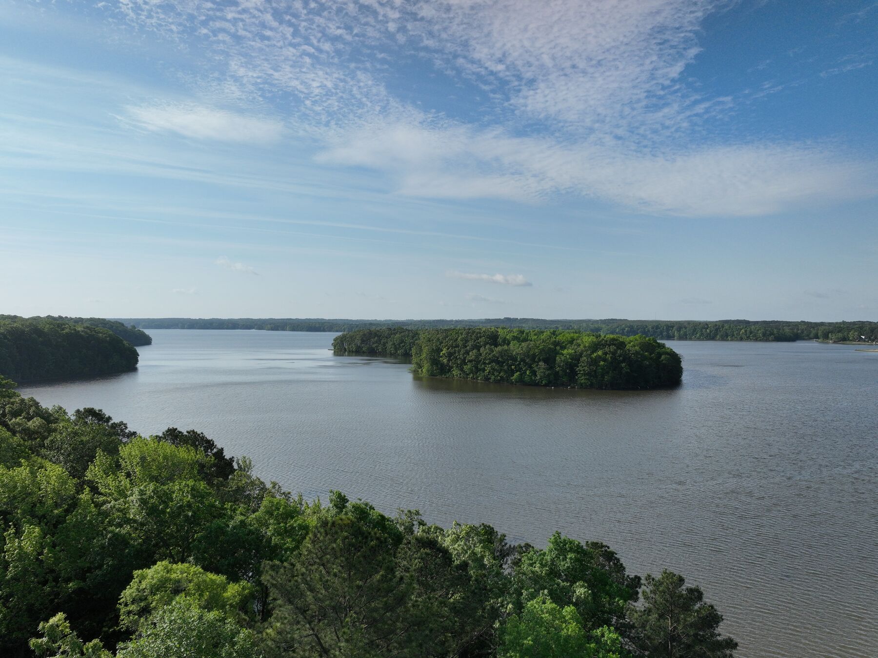 Wide view over the lake and a wooded island from above the shore.