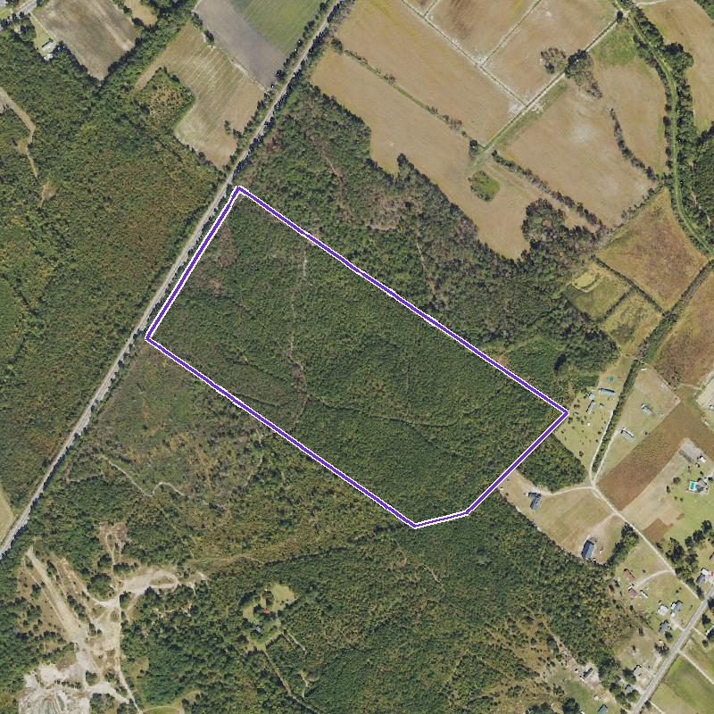 Overhead aerial of a long wooded rectangle outlined, with a railroad and homes along its edges.